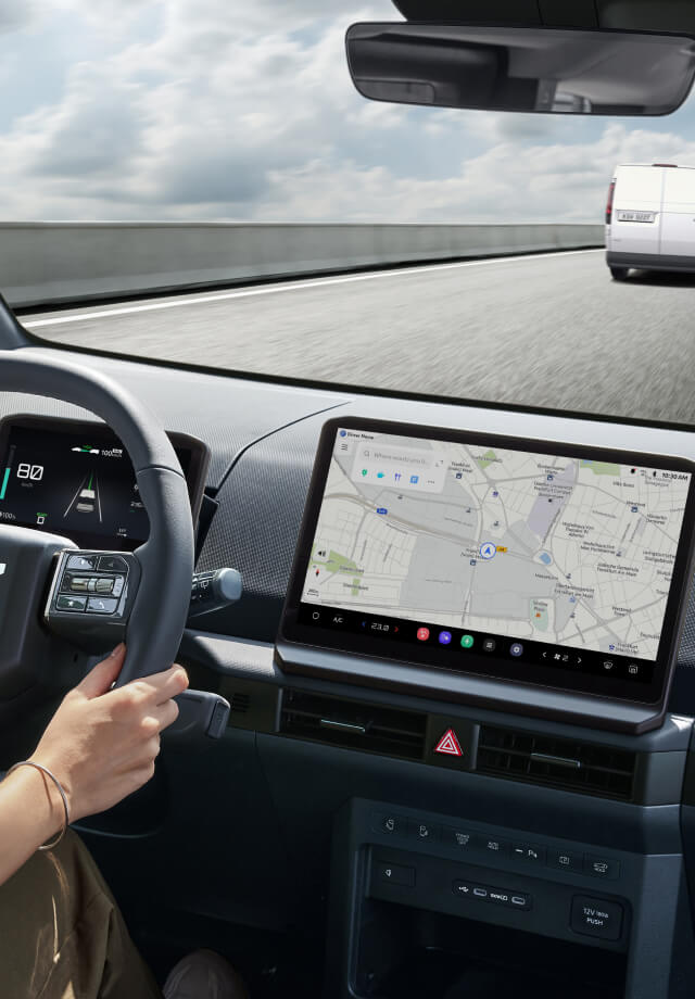 Innenansicht vom Fahrersitz mit Händen am Lenkrad und sichtbarem Navigationsbildschirm.